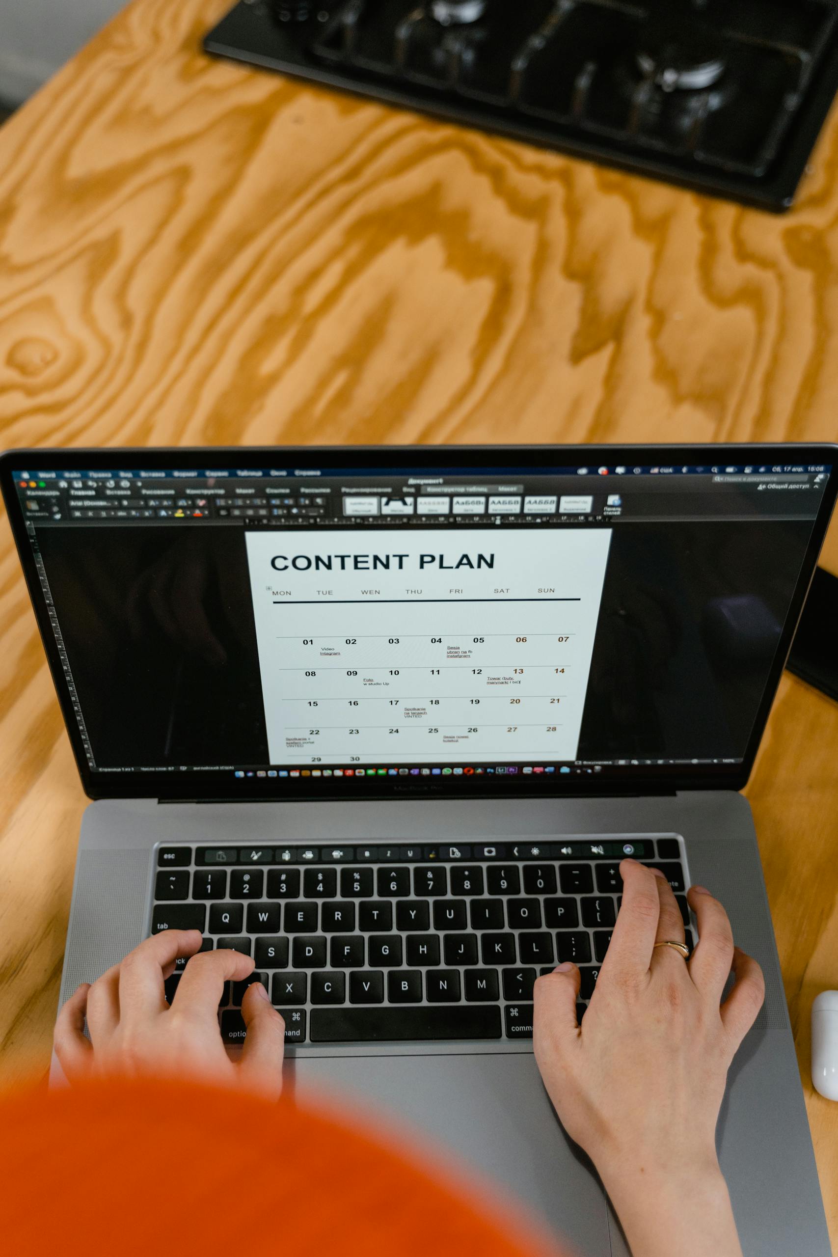 Hands typing on a laptop keyboard displaying a content plan on screen.